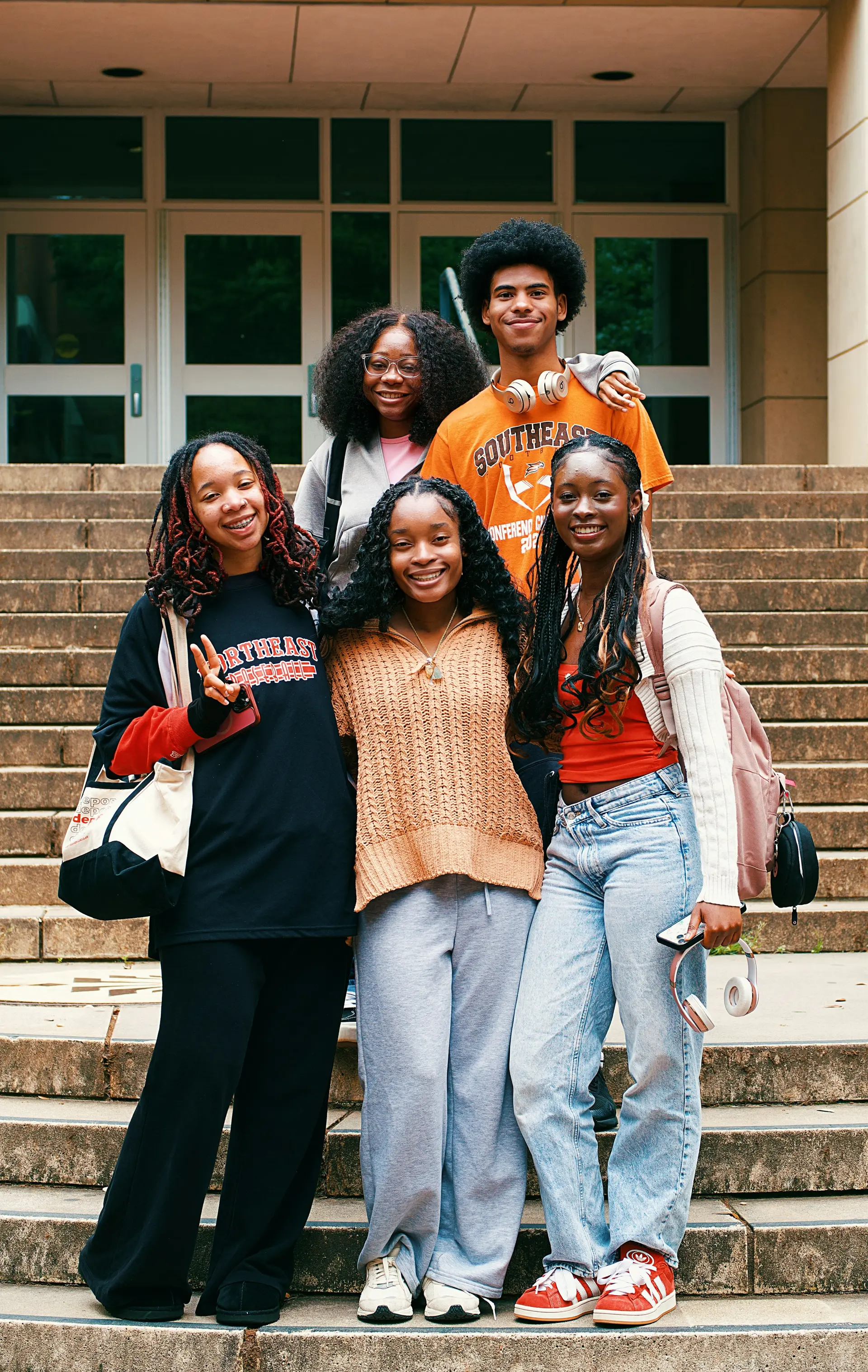 Four young women smiling together on the steps of a college campus