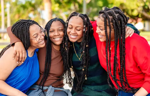 Four smiling teenage girls with braids embracing outdoors