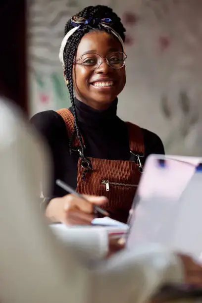 A smiling young woman in glasses taking notes during a group session