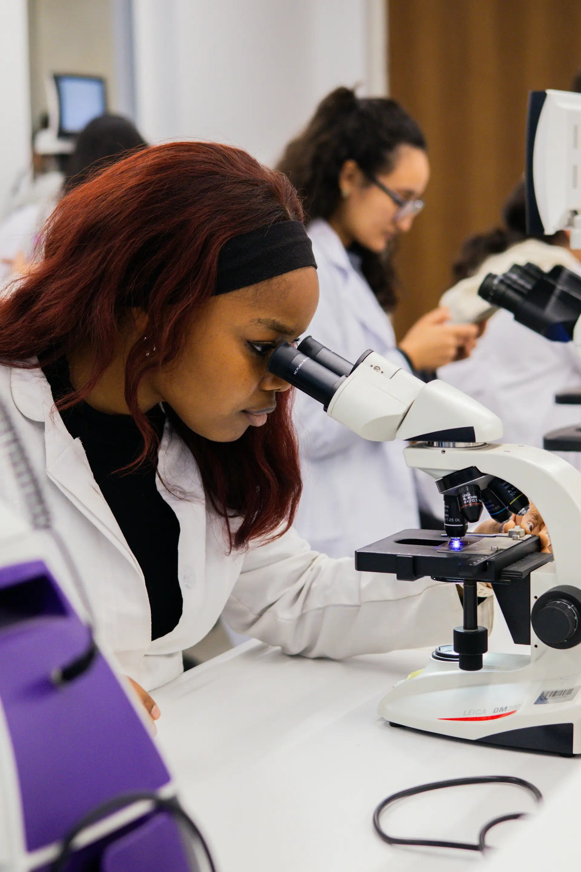 A young woman in a lab coat looking through a microscope
