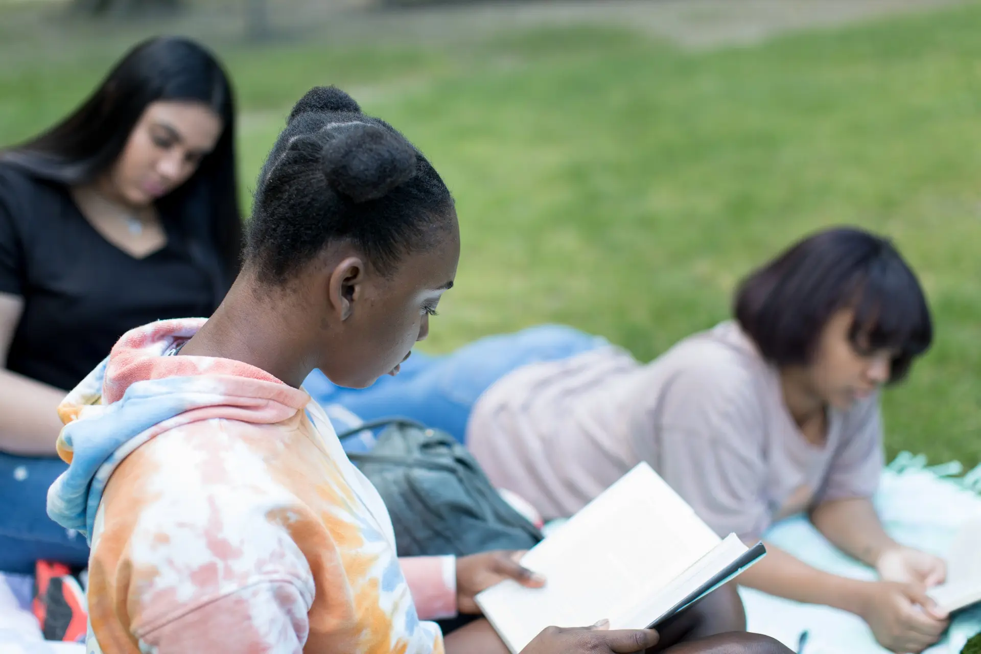 Teenagers reading together outdoors on the grass