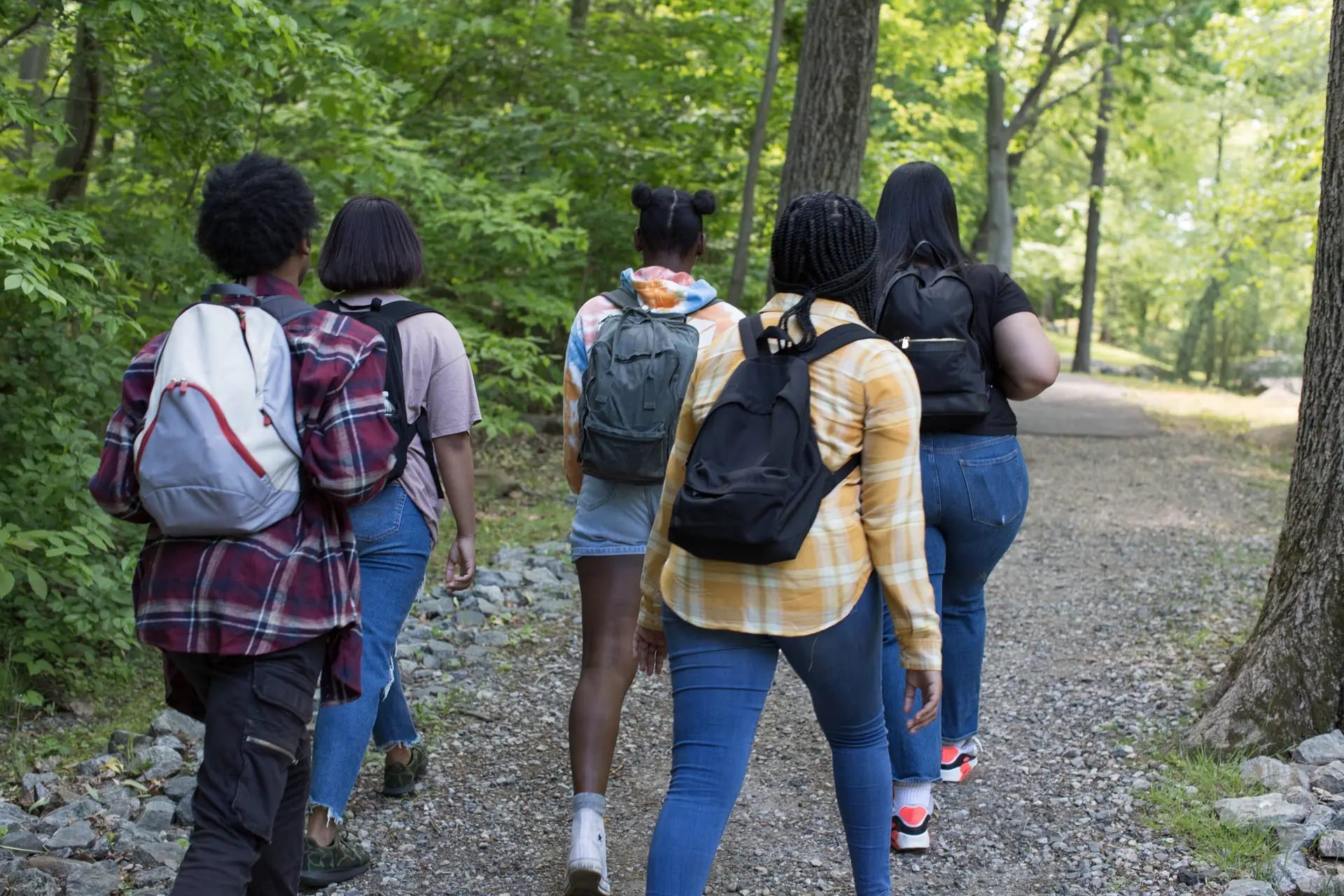 A group of teenagers with backpacks walking a wooded trail