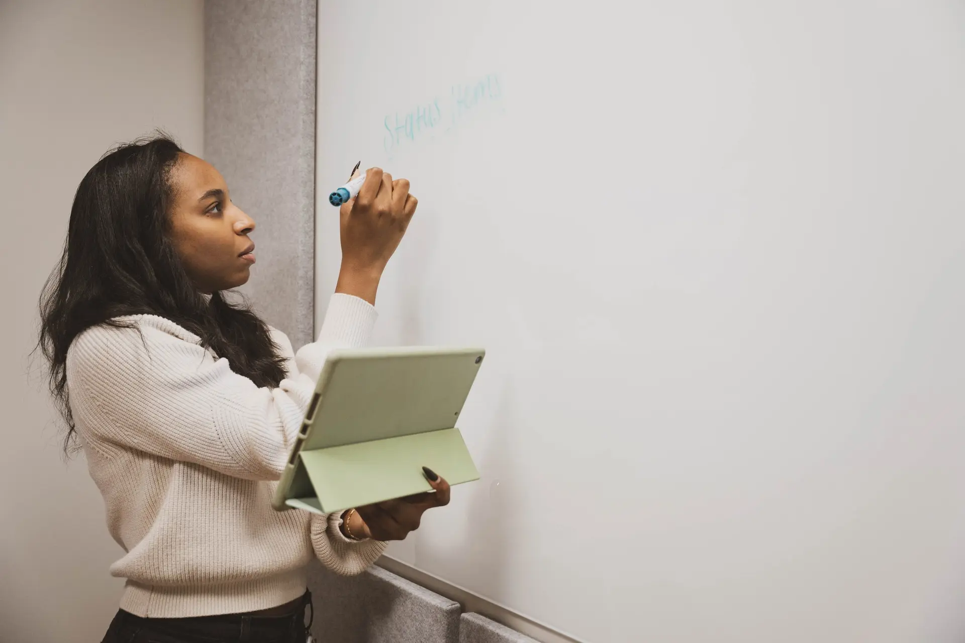 A young woman presenting ideas at a whiteboard while holding a tablet