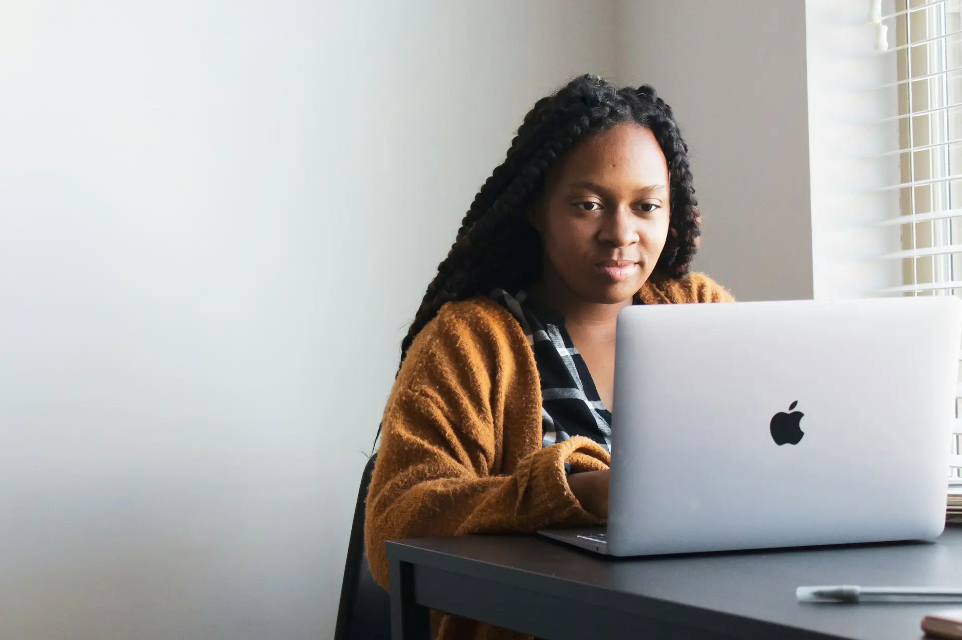 A young woman with braids working on a laptop at a desk